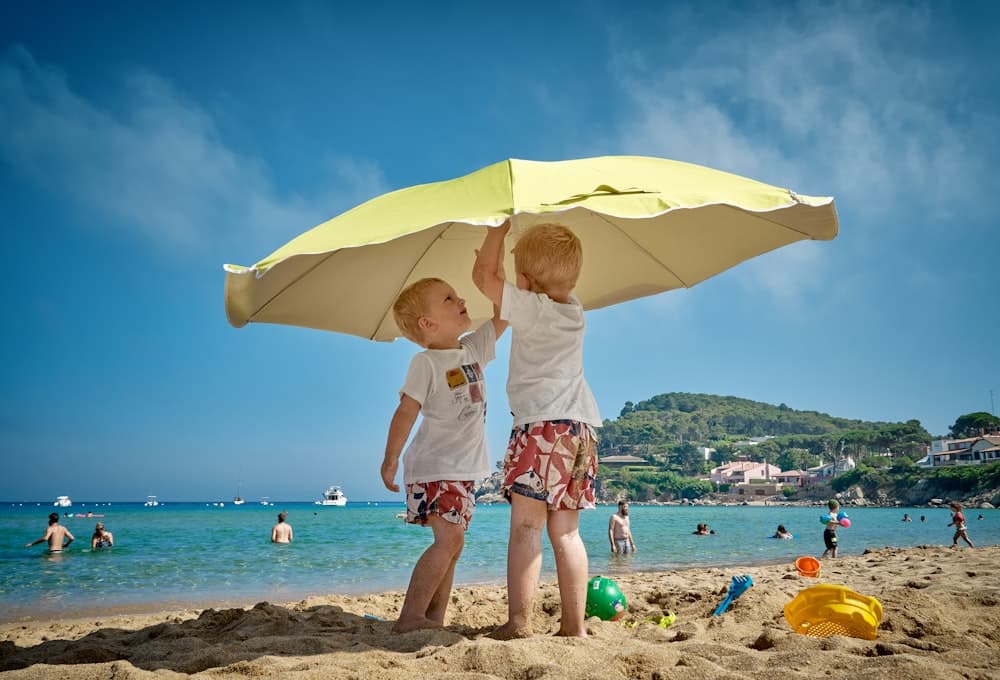 Duas crianças brincando sob um guarda-sol na areia