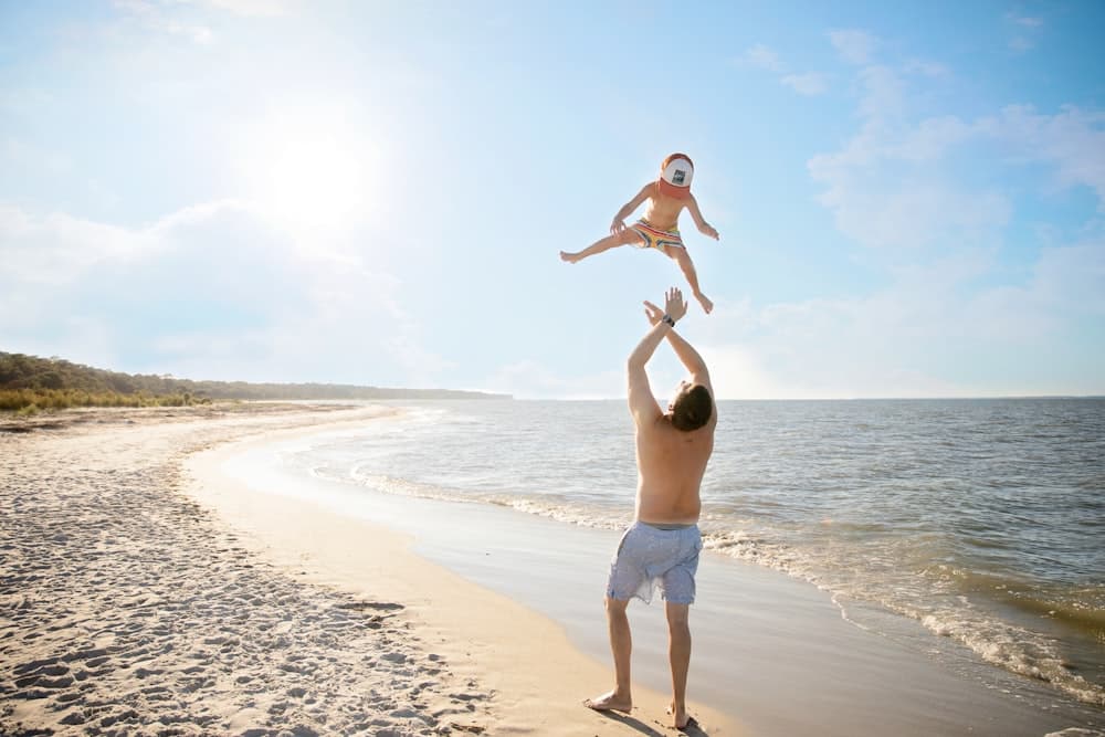 Pai brincando com a filha no colo na praia