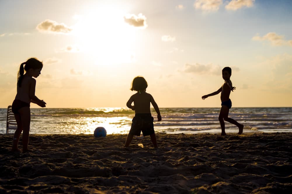 Crianças jogando bola na areia ao entardecer