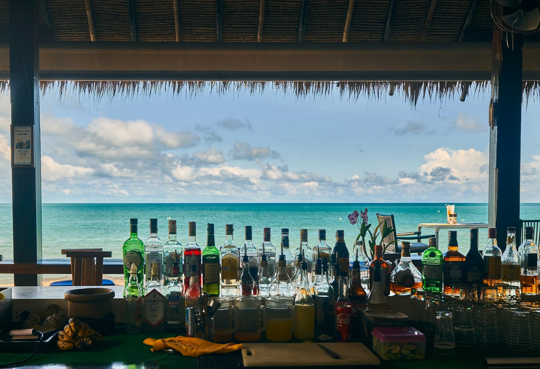 Balcão do Kanoa Beach Bar sob teto de palha, com o mar ao fundo